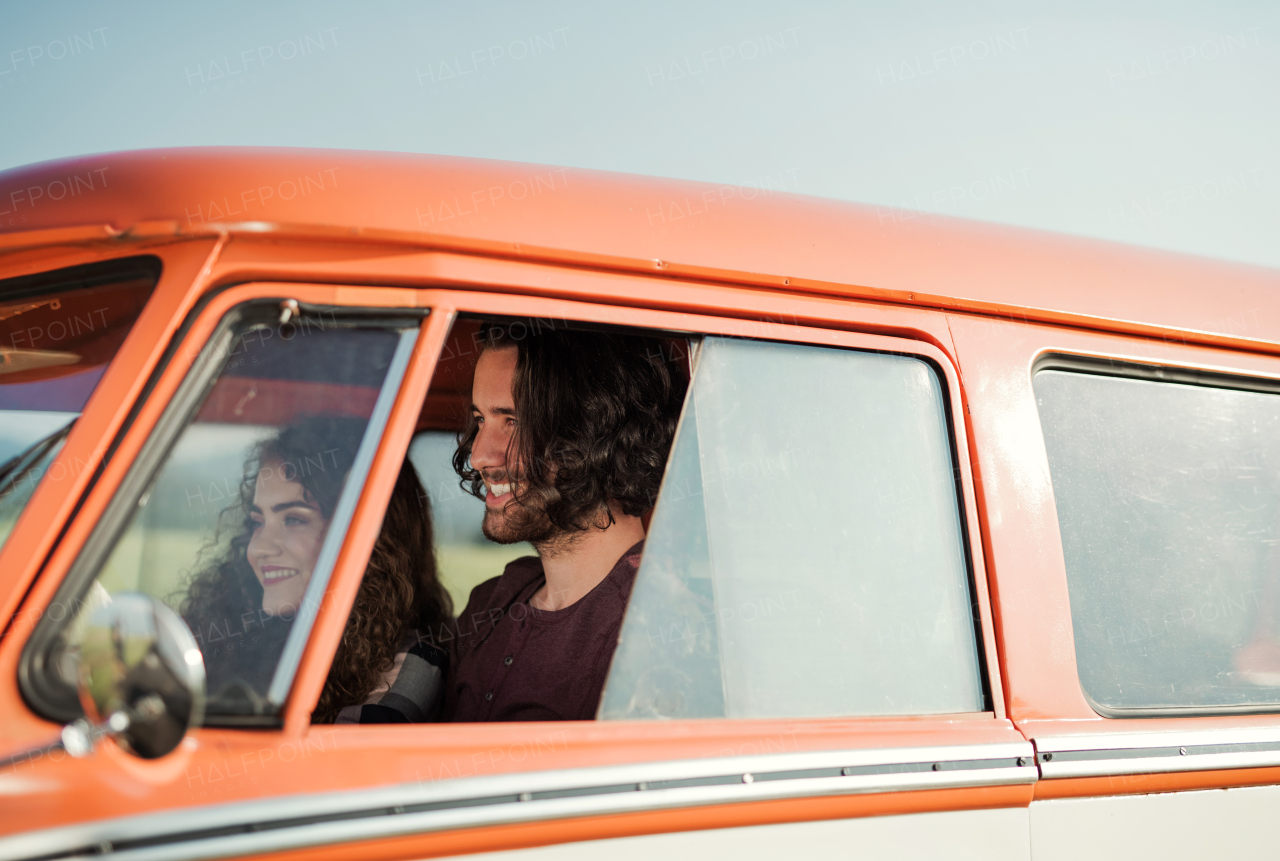 A young couple on a roadtrip through countryside, driving retro minivan.