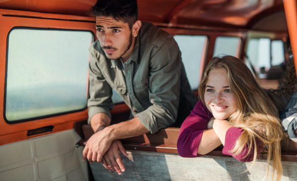 A group of cheerful young friends with a retro minivan on a roadtrip through countryside, looking out of window.