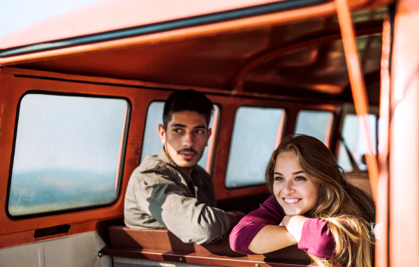 A young couple on a roadtrip through countryside, sitting in retro minivan.