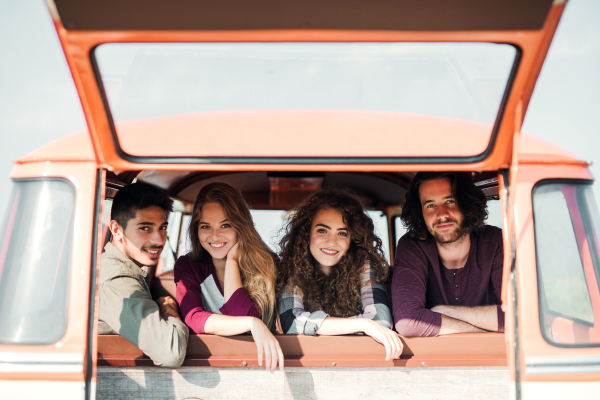 A group of cheerful young friends with a retro minivan on a roadtrip through countryside, looking out of window.