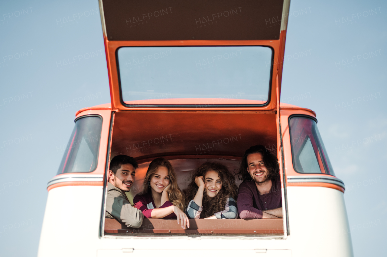 A group of cheerful young friends with a retro minivan on a roadtrip through countryside, looking out of window.