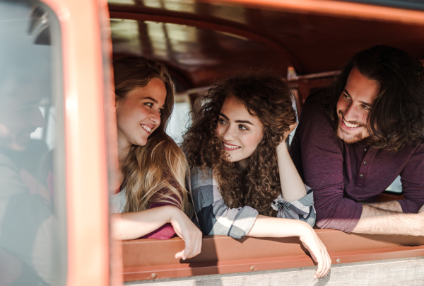 A group of cheerful young friends with a retro minivan on a roadtrip through countryside, talking.