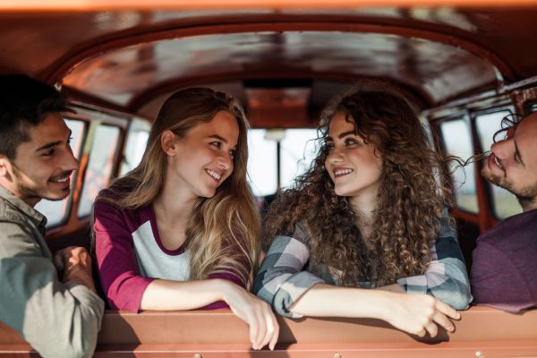 A group of cheerful young friends with a retro minivan on a roadtrip through countryside, sitting in a car.