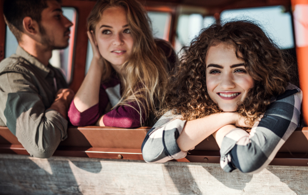 A group of cheerful young friends with a retro minivan on a roadtrip through countryside, looking out of window.