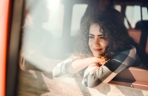 A cheerful young girl looking out of a car on a roadtrip through countryside. Shot through glass.