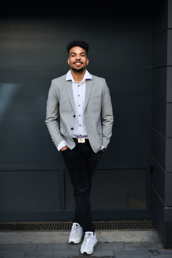 A portrait of young man student standing outdoors in city against black background, looking at camera.