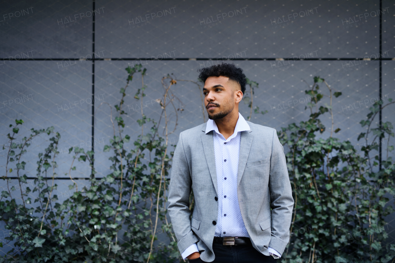 A portrait of young man student standing outdoors in city, hands in pockets.