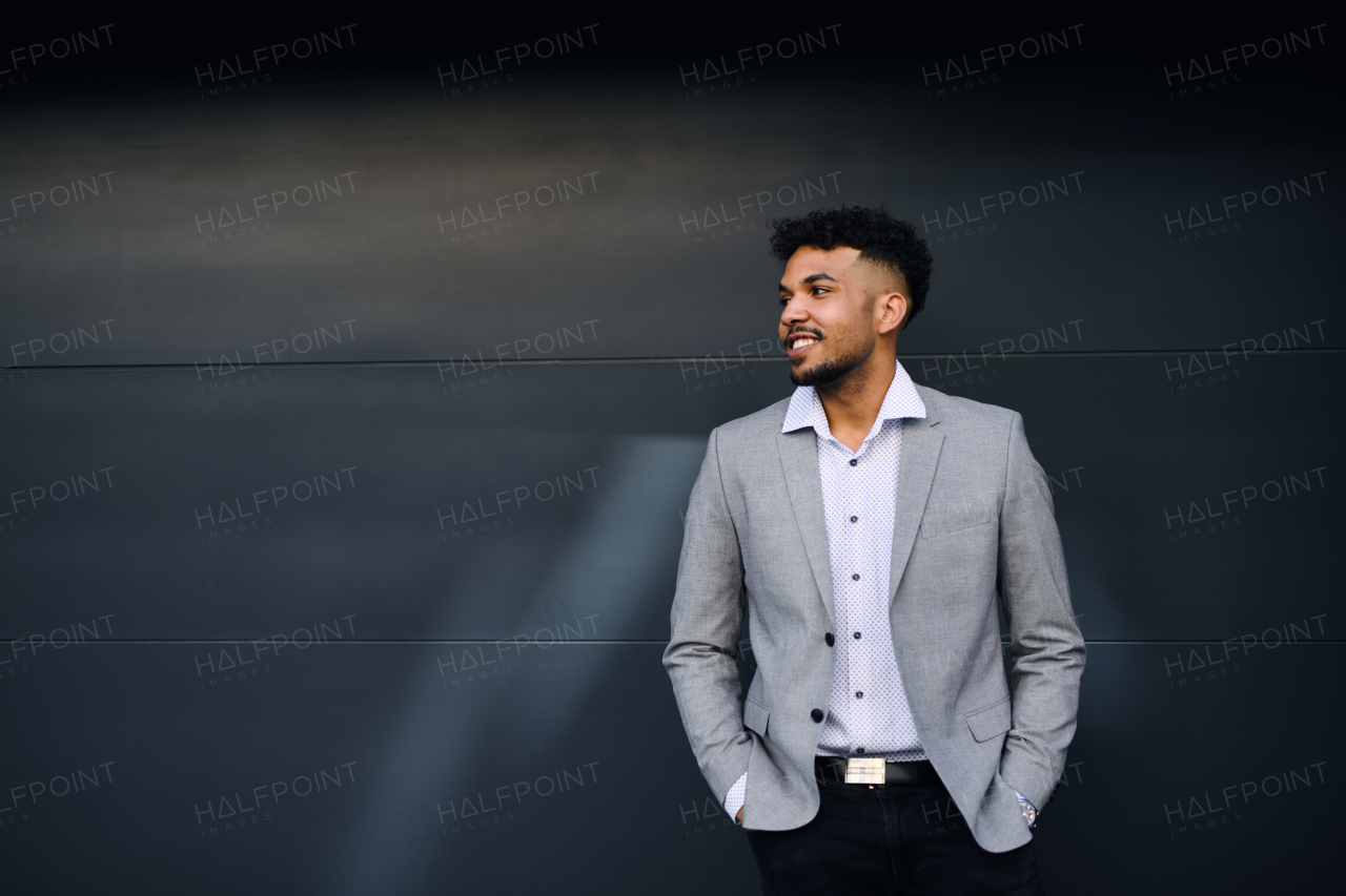 A portrait of young man student standing outdoors in city against black background, hands in pockets.