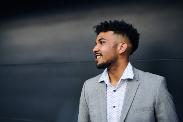 A portrait of young man student standing outdoors in city against black background.