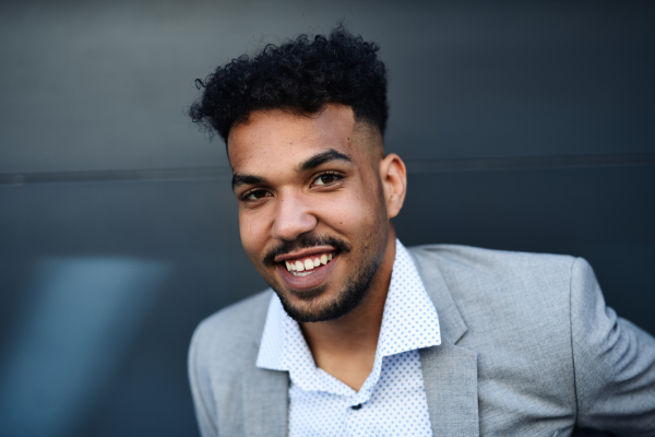 A portrait of young man student standing outdoors in city against black background, looking at camera.