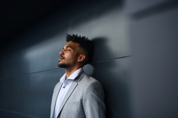 A portrait of young man student standing outdoors in city against black background, eyes closed.