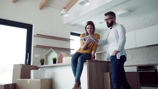 A young happy couple with tablet talking when furnishing new house, a moving in new home concept.