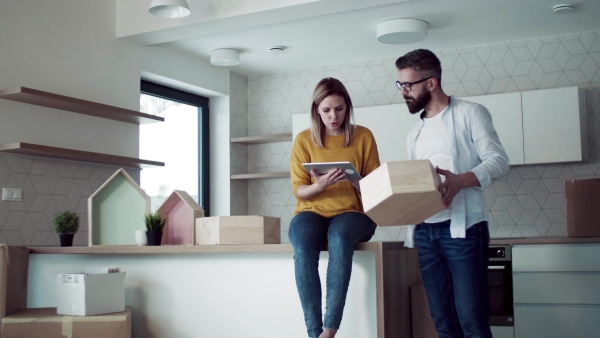 A young happy couple with tablet talking when furnishing new house, a moving in new home concept.