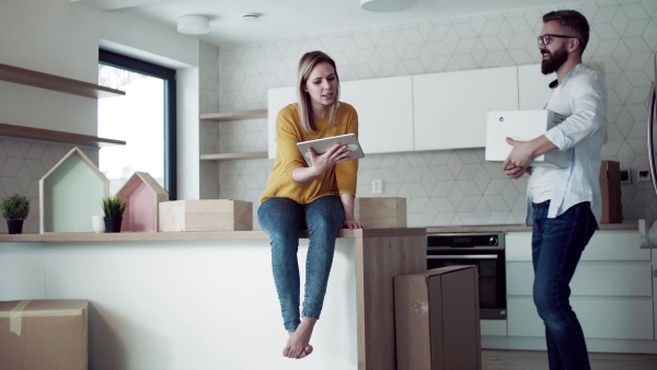 A young happy couple with tablet talking when furnishing new house, a moving in new home concept.