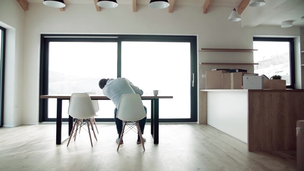 A rear view of mature man sitting at the table in new home, using tablet. Slow motion.