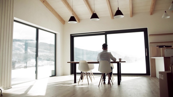 A rear view of mature man sitting at the table in new home, using tablet. Slow motion.