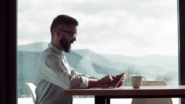 A mature man with glasses sitting at the table in new home, using tablet. Slow motion.