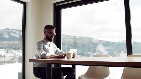 A mature man with glasses sitting at the table in new home, using tablet. Slow motion.