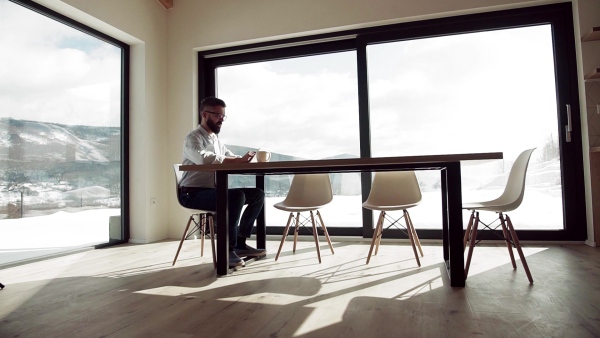 A mature man with glasses sitting at the table in new home, using tablet. Slow motion.