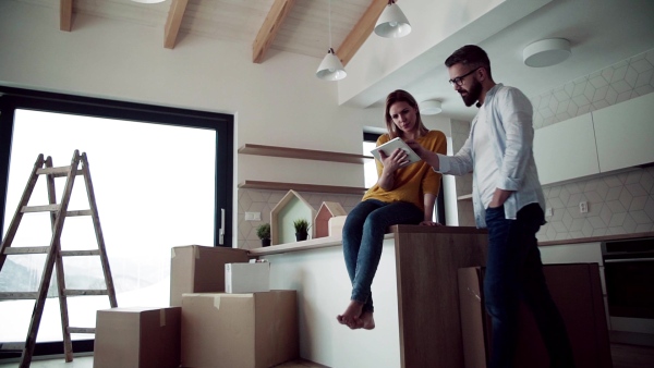 A young happy couple with tablet talking when furnishing new house, a moving in new home concept. Slow motion.