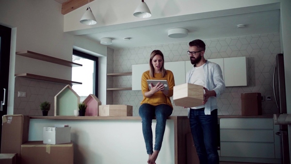 A young happy couple with tablet talking when furnishing new house, a moving in new home concept. Slow motion.