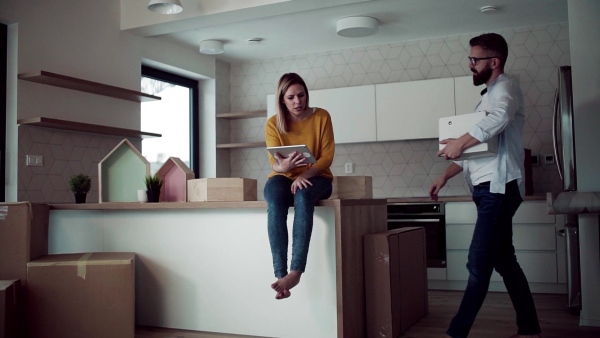 A young happy couple with tablet talking when furnishing new house, a moving in new home concept. Slow motion.