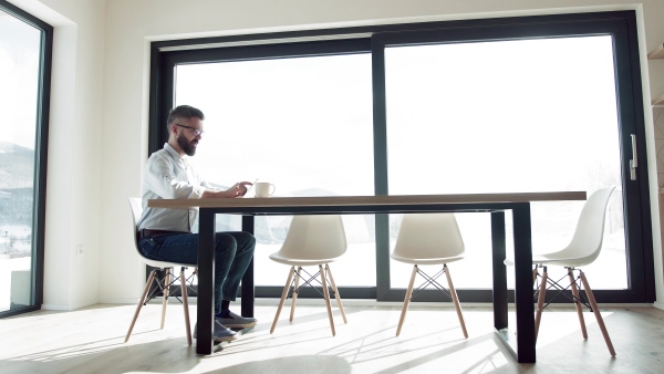 A mature man with glasses sitting at the table in new home, using tablet.