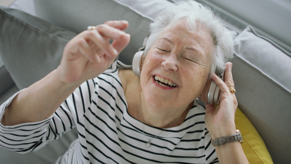 A senior woman at home with smartphone and headphones listening to music.