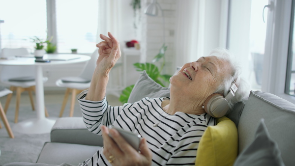 A senior woman at home with smartphone and headphones listening to music.