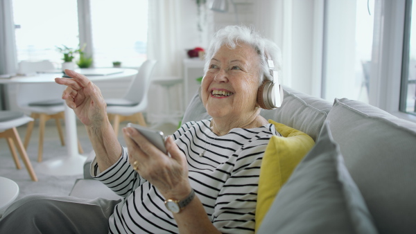 A senior woman at home with smartphone and headphones listening to music.