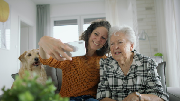 An adult daughter taking selfie with her mother indoors at home.