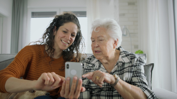 An adult daughter helping senior mother with smarphone, explaining.