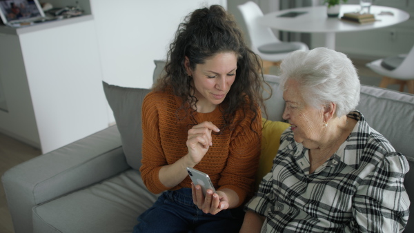 An adult daughter helping senior mother with smarphone, explaining.