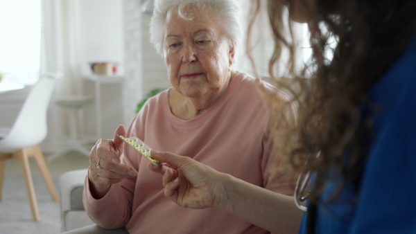 A healthcare worker or caregiver visiting senior woman indoors at home, explaining how to use medication.