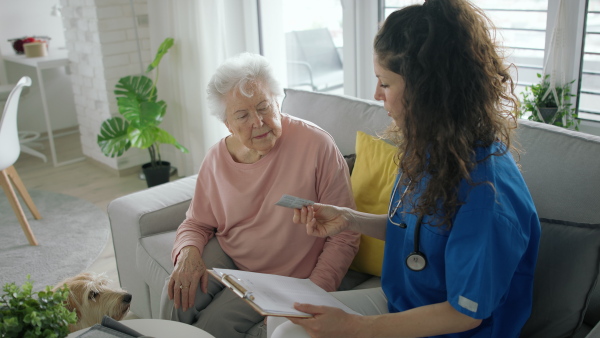 A healthcare worker or caregiver visiting senior woman indoors at home, explaining how to use medication.