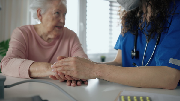 A close up of healthcare worker or caregiver visiting senior woman indoors at home, comforting her.