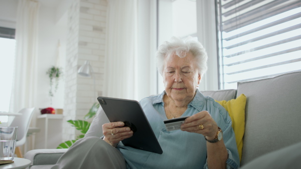 A senior woman at home with tablet paying by credit card, looking at camera. Online shopping concept.