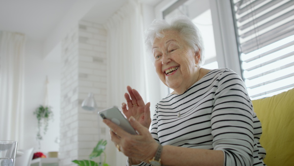 A senior woman at home with smartphone having an video call.