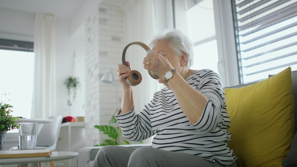 A senior woman at home with smartphone and headphones listening to music.