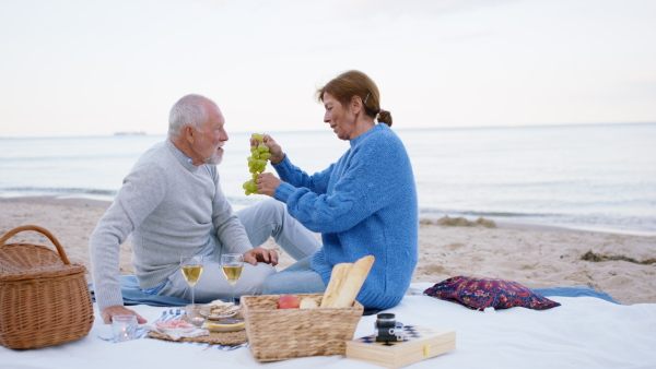 A happy senior couple in love outdoors on beach, sitting and having a picnic.