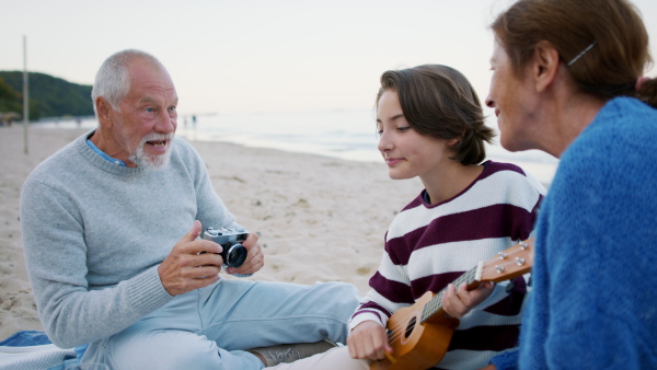 A happy senior couple with granddaughter on beach, having a picnic and taking pictures.