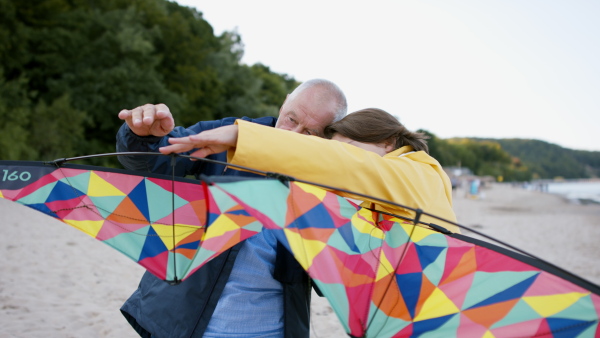 A grandfather with granddaughter on walk on beach at morning, preparing a kite.