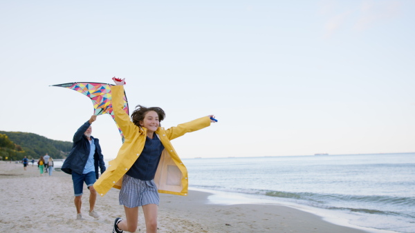 A grandfather with granddaughter on walk on beach at morning, running with a kite.