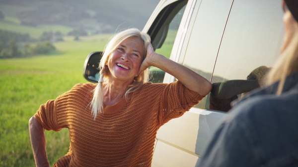 An old woman standing by car with her best friend. outdoors in nature, caravan trip holiday.