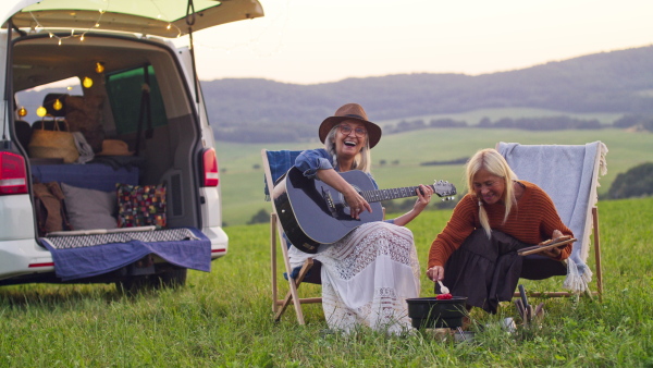 An old women eating and playing guitar, resting in nature, caravan trip holiday.