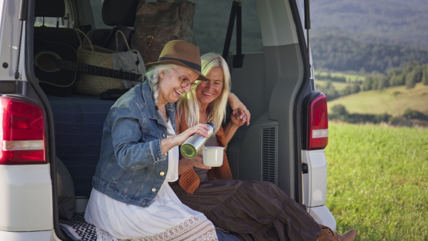 A senior women friends resting and drinking tea, caravan trip holiday.