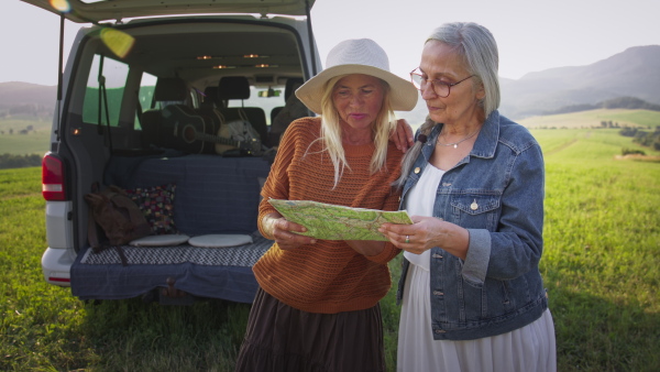 Senior women friends using map outdoors in nature, a caravan trip holiday.