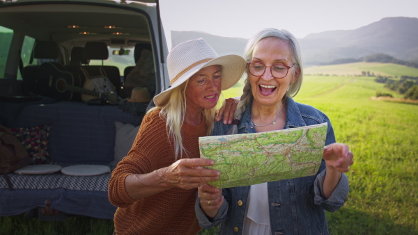 Senior women friends using map outdoors in nature, a caravan trip holiday.