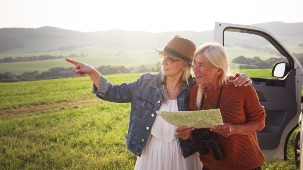 Senior women friends using map outdoors in nature, a caravan trip holiday.