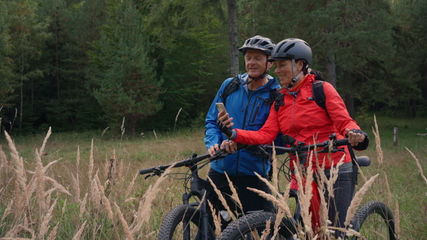 A senior couple bikers using smartphone outdoors in forest in autumn day.